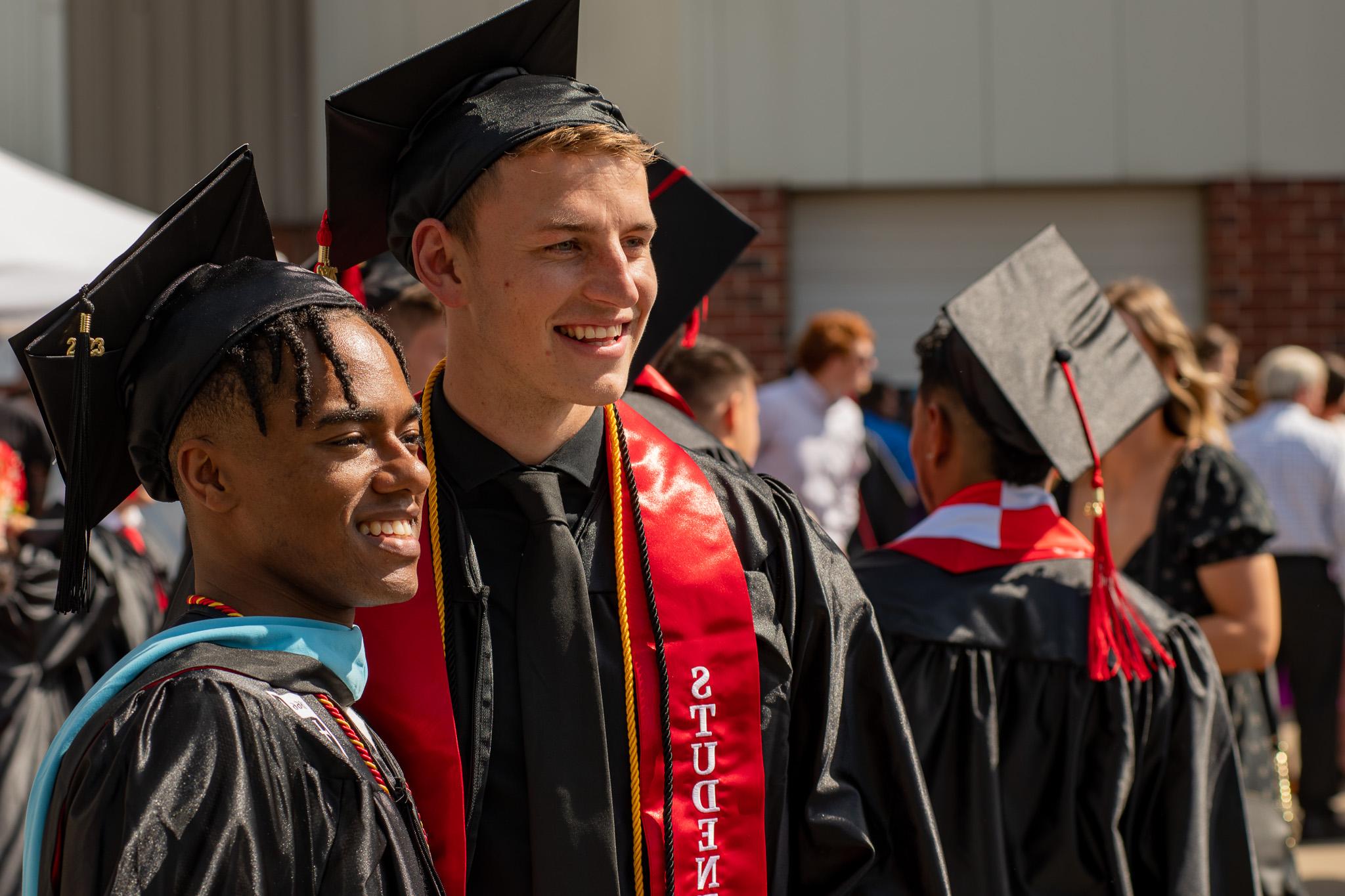 Roberts Wesleyan University graduates smile and pose for a photo at an outdoor commencement ceremony.